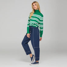 Load image into Gallery viewer, Woman wearing a green and white striped sweater with blue pants on a gray background