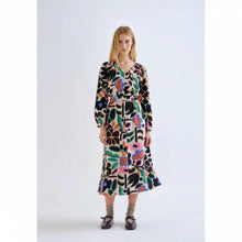 Load image into Gallery viewer, A woman stands against a plain light gray studio background wearing a long-sleeve midi dress with an abstract multicolor print. The dress has a black base with large organic shapes in pink, green, orange, blue, and cream.
