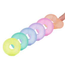 Load image into Gallery viewer, Six pastel-colored donut-shaped silicone items arranged in a diagonal line on a light gray background, with a hand partially visible at the far right holding one peach-colored piece.

